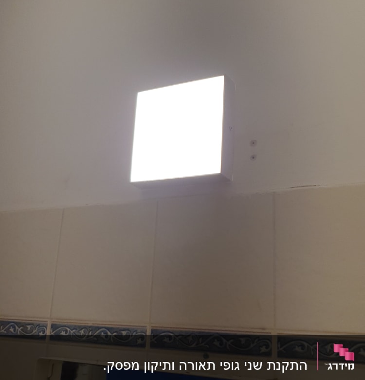 מנורת קיר מרובעת מוארת על קיר לבן